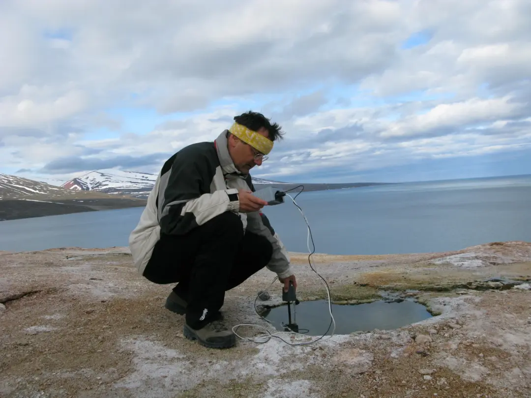 Uno scienziato inginocchiato analizza con uno strumento l’acqua contenuta in una pozza vicino al mare